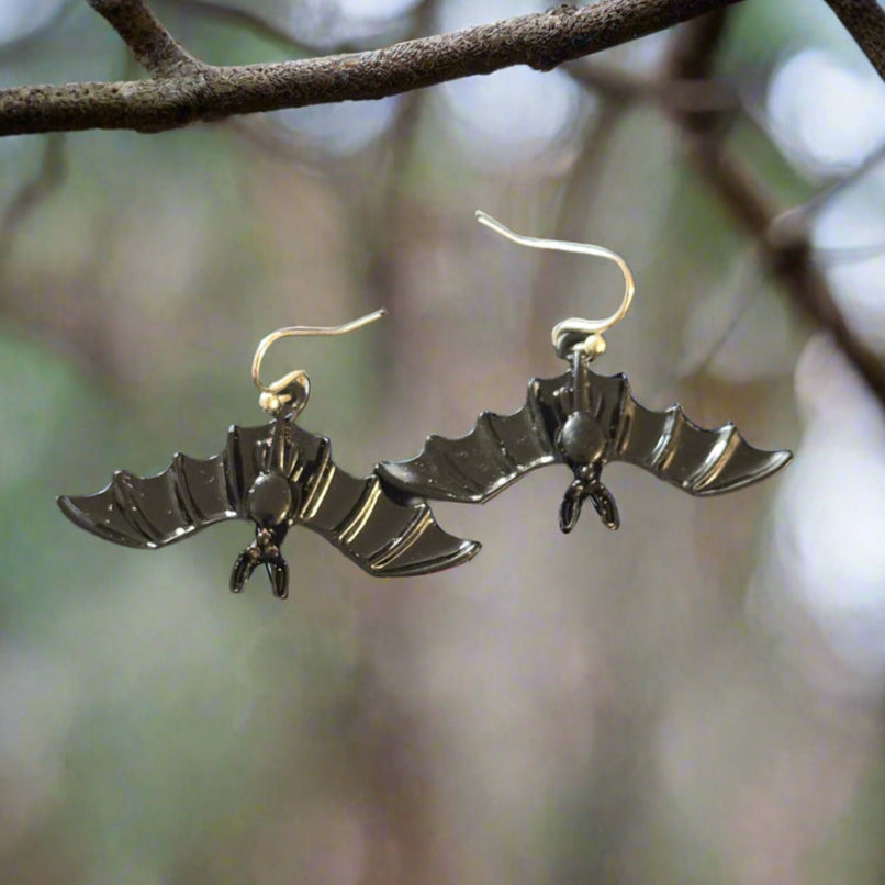 Midnight Wings Earrings featuring black enamel bat charms swinging upside down from nickel and lead-free steel hooks, displayed on a soft background