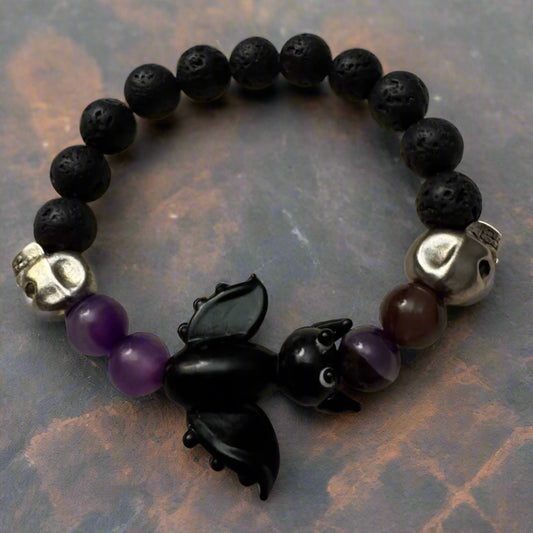 Eternal Void Lava & Amethyst Bracelet with black lava beads, vibrant amethyst stones, a black bat centerpiece, silver skull charms, and purple amethyst beads, displayed on a dark background