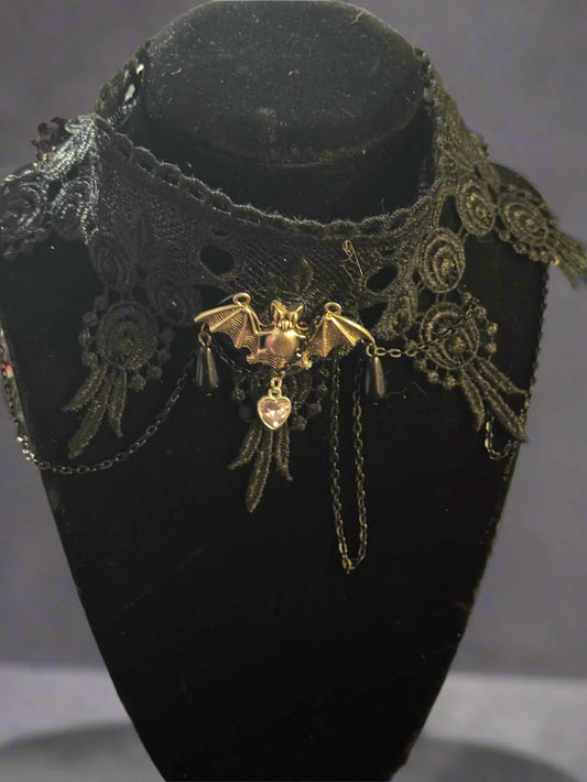Nocturnal Embrace Choker featuring a sultry black lace design with a silver bat charm at the center, displayed on a dark background