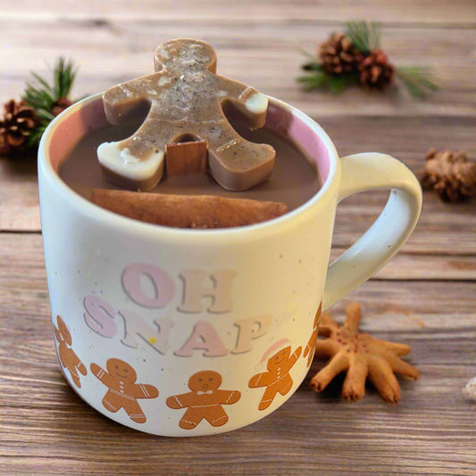 Oh Snap! Gingerbread Candle Mug with cream-colored ceramic mug featuring gingerbread cookies and the phrase “Oh Snap!”; hot chocolate-colored soy wax, a gingerbread-shaped wax melt topper, a cinnamon stick garnish, and a crackling wood wick, displayed on a soft background