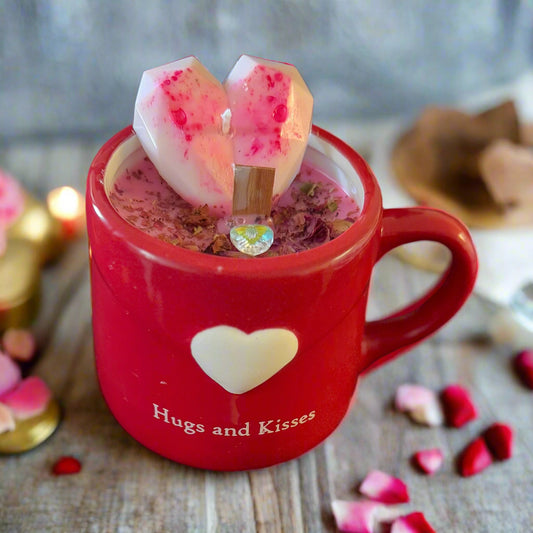 Sweetheart Glow Candle in a red stoneware mug with a white heart labeled “Hugs and Kisses,” filled with pink soy wax, topped with rose petals, a clear prism heart charm, and a geometric heart-shaped wax topper, featuring a crackling wood wick